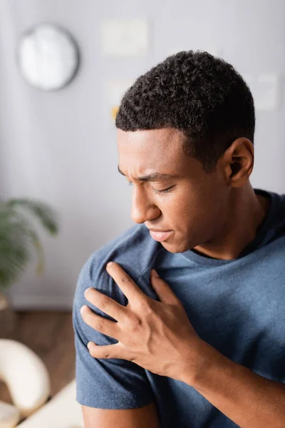 Injured african american man touching shoulder in clinic — Stock Photo