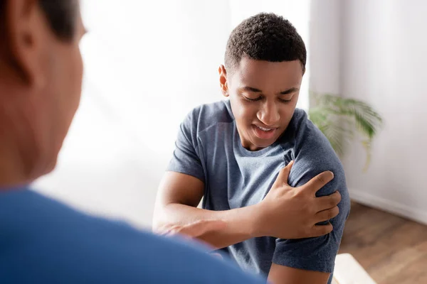 Blessé afro-américain toucher la main près du médecin sur flou au premier plan — Photo de stock