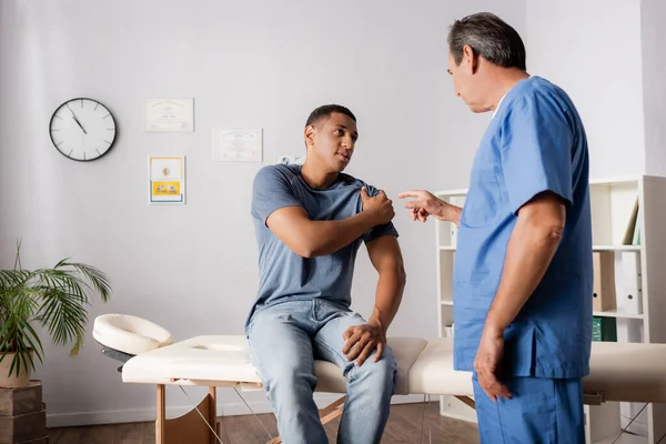 Medico che punta con il dito al braccio ferito del paziente afroamericano — Foto stock