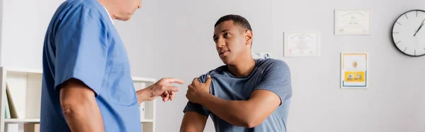 Médico señalando con el dedo al brazo lesionado del paciente afroamericano, pancarta - foto de stock