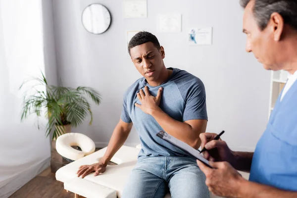 Doctor writing prescription near african american patient in clinic — Stock Photo