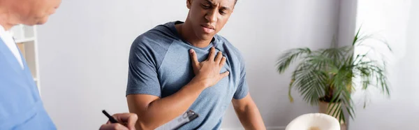 Uomo afroamericano toccando petto vicino medico con penna, banner — Foto stock