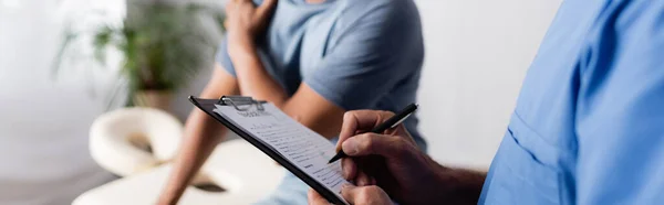 Abgeschnittene Ansicht des Arztes, der Rezept in der Nähe eines afrikanisch-amerikanischen Patienten in der Klinik schreibt, Banner — Stockfoto