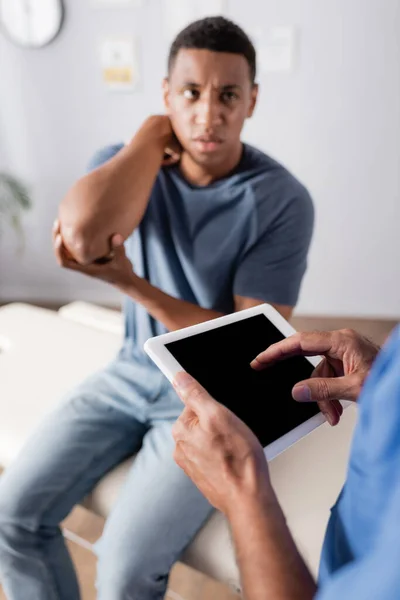 Arzt zeigt mit Finger auf digitales Tablet mit leerem Bildschirm nahe afrikanisch-amerikanischem Patienten auf verschwommenem Hintergrund — Stockfoto