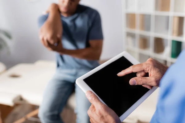 Vista recortada del médico apuntando con el dedo a la tableta digital cerca del paciente afroamericano sobre fondo borroso - foto de stock