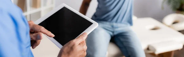 Teilbild eines reifen Arztes mit digitalem Tablet in der Nähe eines afrikanisch-amerikanischen Patienten auf verschwommenem Hintergrund, Banner — Stockfoto