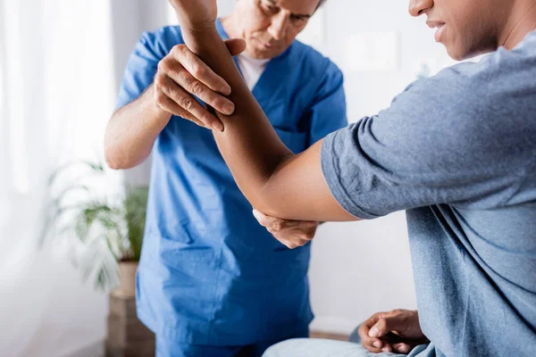 Chiropraktiker arbeitet mit verletztem Arm eines Afroamerikaners in Klinik — Stockfoto