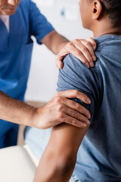 Partial view of chiropractor working with injured african american man in clinic — Stock Photo