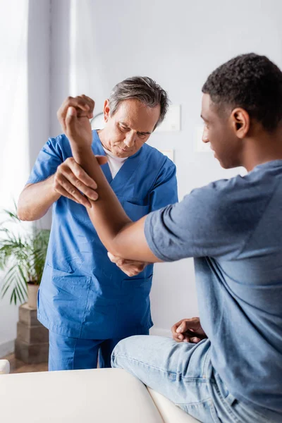 Chiropraticien travaillant avec le bras blessé de l'homme afro-américain en clinique — Photo de stock