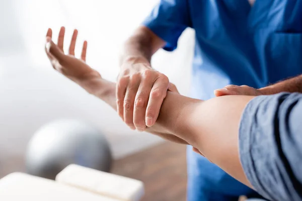 Cropped view of chiropractor working with injured arm of african american man in clinic — Stock Photo