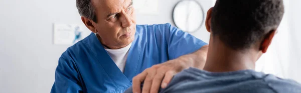 Chiropractor working with injured arm of african american man on blurred foreground, banner — Stock Photo