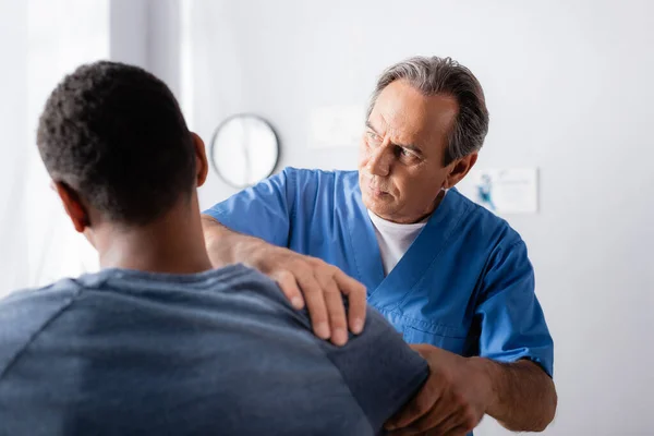 Chiropracteur travaillant avec le bras blessé de l'homme afro-américain au premier plan flou — Photo de stock