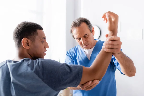 Therapist working with injured african american man on blurred foreground in clinic — Stock Photo