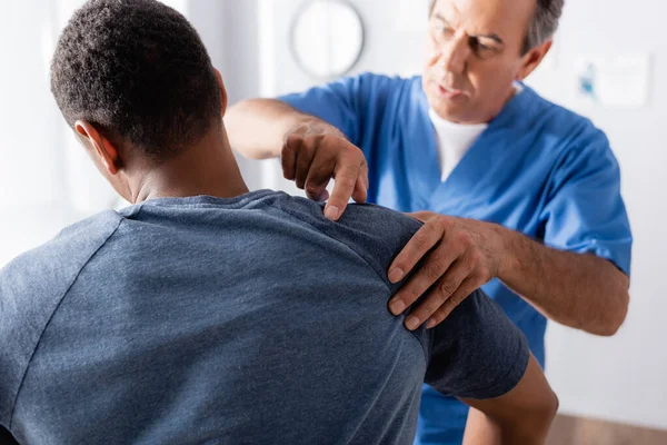 Terapeuta borroso trabajando con hombre afroamericano en clínica - foto de stock