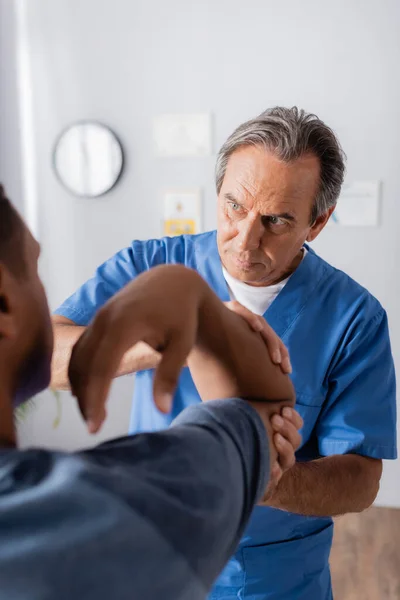 Doctor trabajando con lesionado afroamericano hombre en borrosa primer plano - foto de stock