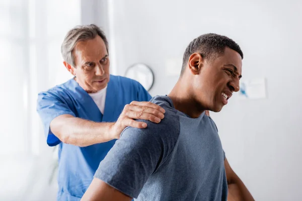 Médecin travaillant avec un homme afro-américain blessé souffrant de douleur à la clinique — Photo de stock