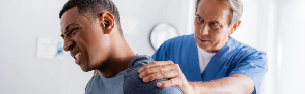 Terapeuta che lavora con l'uomo afroamericano ferito che soffre di dolore, striscione — Foto stock