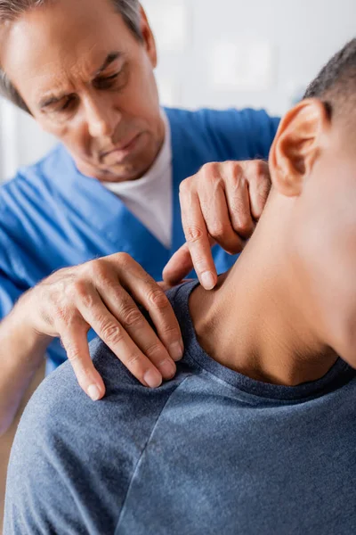 Terapeuta que trabaja con un paciente afroamericano lesionado que sufre de dolor - foto de stock