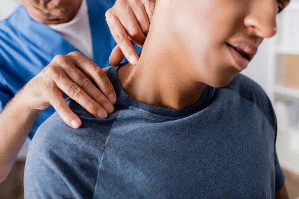 Vista ritagliata del massaggiatore massaggiare ferito paziente africano americano in clinica — Foto stock
