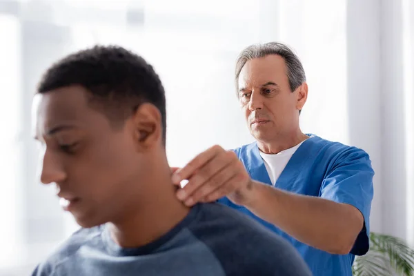 Masseur massaging injured neck of african american patient on blurred foreground — Stock Photo