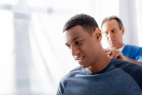 Terapeuta borrosa masajeando paciente afroamericano en clínica - foto de stock