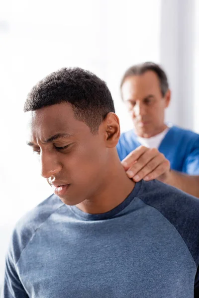 Quiropráctico borroso trabajando con paciente afroamericano en clínica - foto de stock