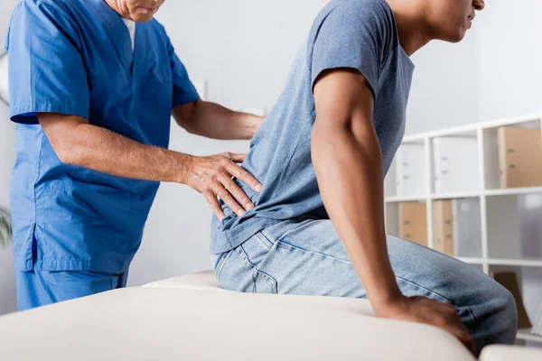 Cropped view of mature chiropractor working with african american man — Stock Photo