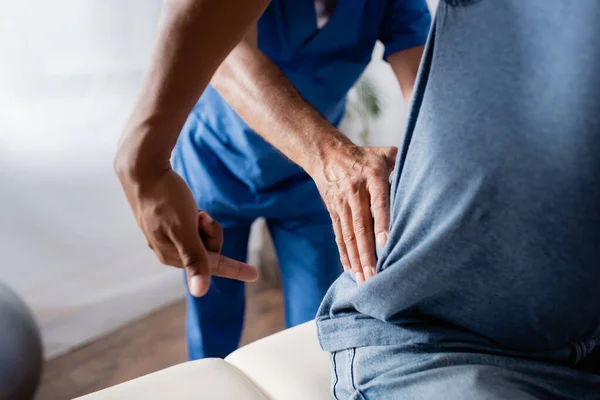 Vue recadrée d'un chiropraticien mature travaillant avec un patient afro-américain — Photo de stock