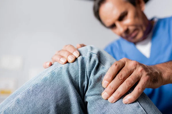 Blurred masseur working with injured knee of patient in clinic — Stock Photo