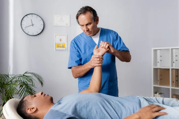 Chiropraktiker arbeitet mit verletztem Arm eines Afroamerikaners auf Massagetisch — Stockfoto