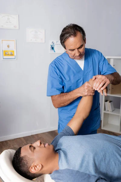 Quiropráctico trabajando con brazo lesionado de paciente afroamericano en mesa de masaje - foto de stock