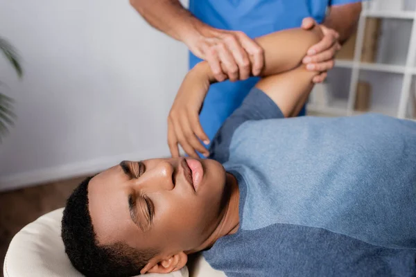 Chiropraticien travaillant avec le bras blessé du jeune patient afro-américain sur table de massage — Photo de stock