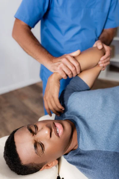 Chiropractor working with arm of injured african american patient on massage table — Stock Photo