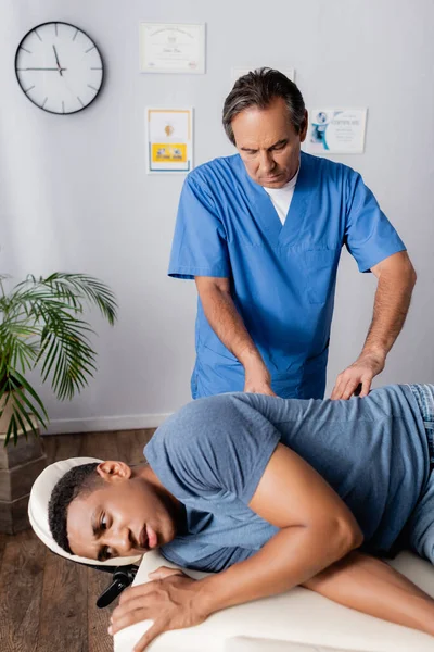 Middle aged chiropractor working with african american patient on massage table — Stock Photo