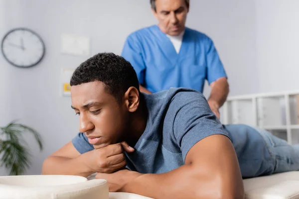 Chiropratico di mezza età che lavora con un giovane paziente afroamericano sul lettino da massaggio — Foto stock