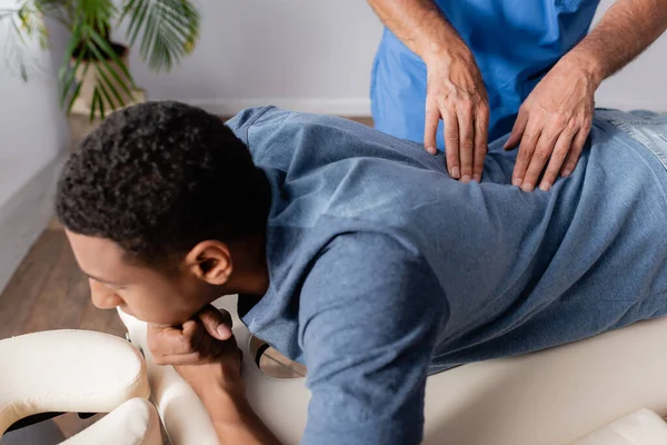 Quiroprático trabalhando com jovem paciente afro-americano na mesa de massagem na clínica — Fotografia de Stock