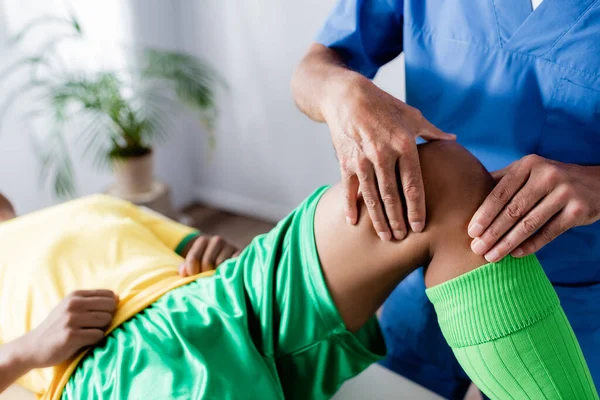 Visão recortada do massagista massageando o joelho do esportista afro-americano — Fotografia de Stock