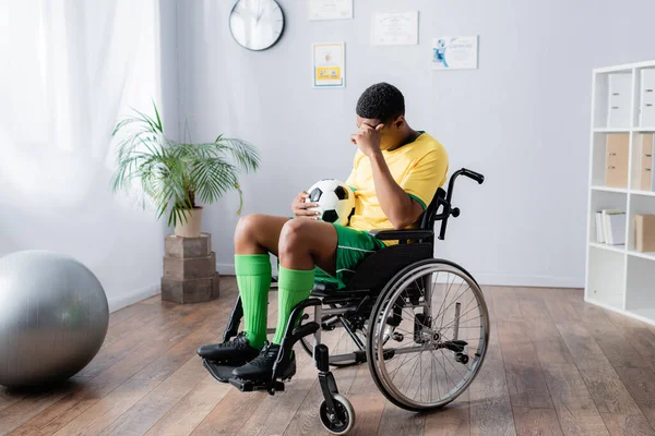 Chateado desativado Africano americano desportista em cadeira de rodas segurando futebol — Fotografia de Stock