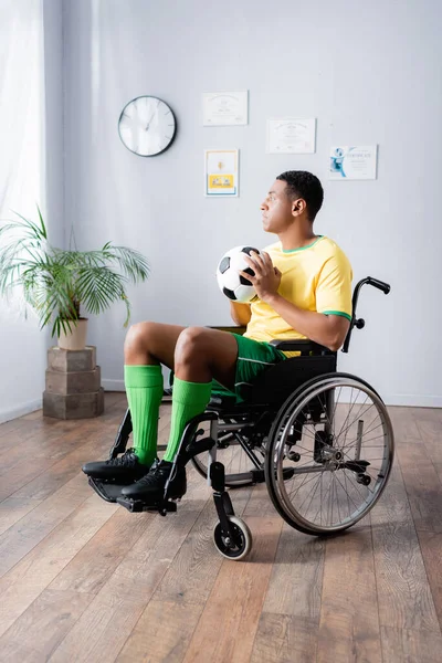 Disabled african american sportsman in wheelchair holding football — Stock Photo