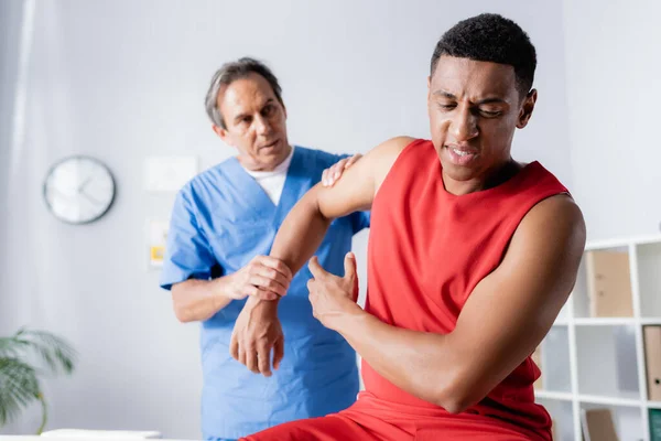 Chiropracteur mature travaillant avec un homme afro-américain blessé en vêtements de sport — Photo de stock