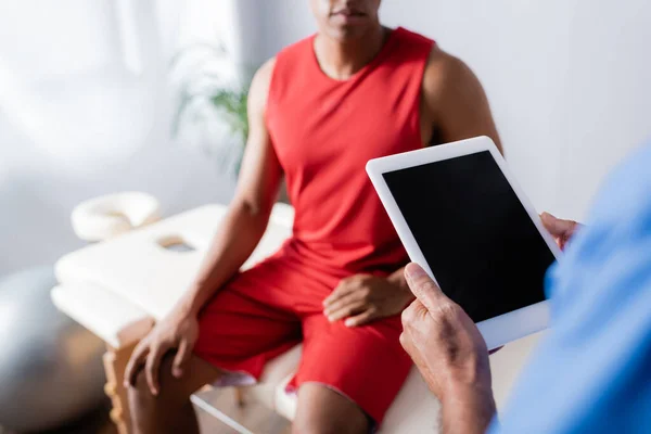 Cropped view of doctor holding digital tablet with blank screen near african american patient in sportswear on blurred background — Stock Photo