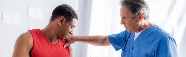 Quiropráctico maduro que trabaja con el paciente afroamericano en ropa deportiva, bandera - foto de stock