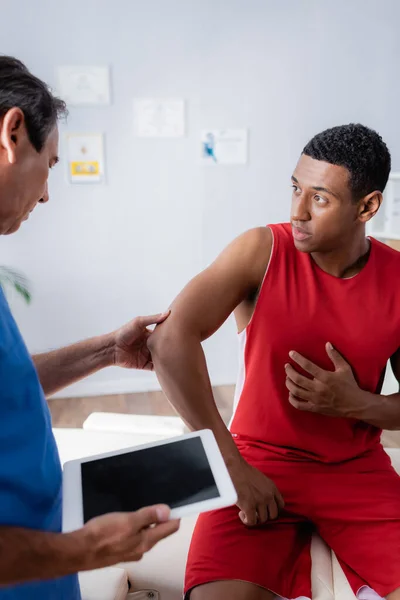 Doctor holding digital tablet with blank screen near worried african american man in sportswear — Stock Photo