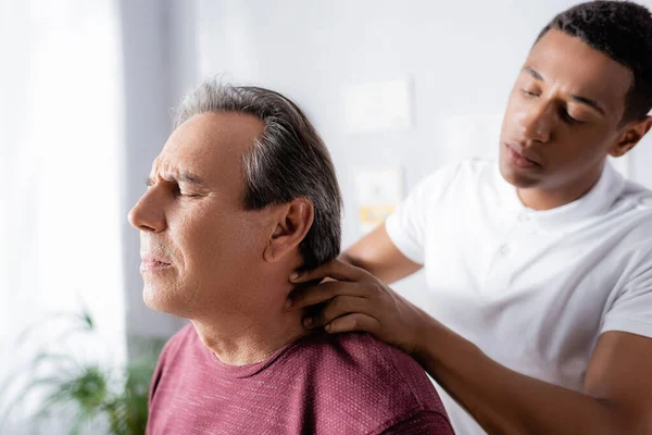 Africano americano fisioterapeuta masaje cuello de maduro hombre en clínica - foto de stock