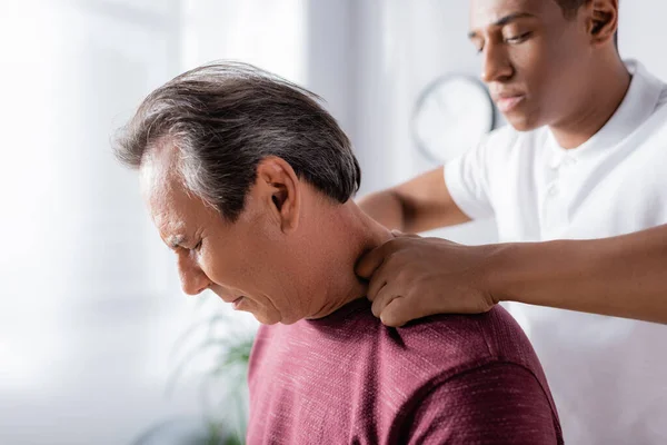 Afrikanische amerikanische Physiotherapeutin massiert Mann mittleren Alters in Klinik — Stockfoto