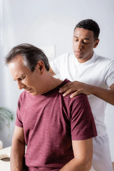 African american physiotherapist massaging middle aged man with closed eyes in clinic — Stock Photo