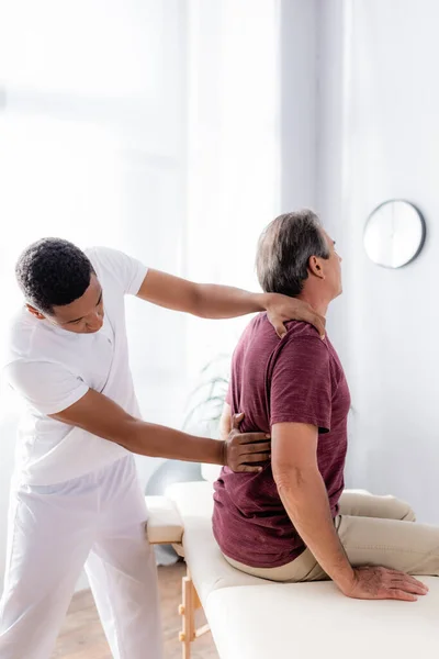 Quiropráctico afroamericano trabajando con la espalda de hombre de mediana edad en la clínica - foto de stock