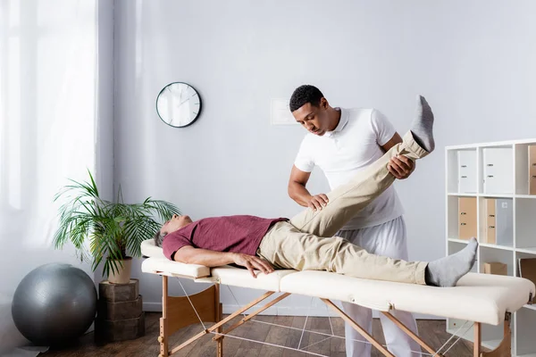 Chiropraticien afro-américain travaillant avec un homme d'âge moyen dans une clinique moderne — Photo de stock