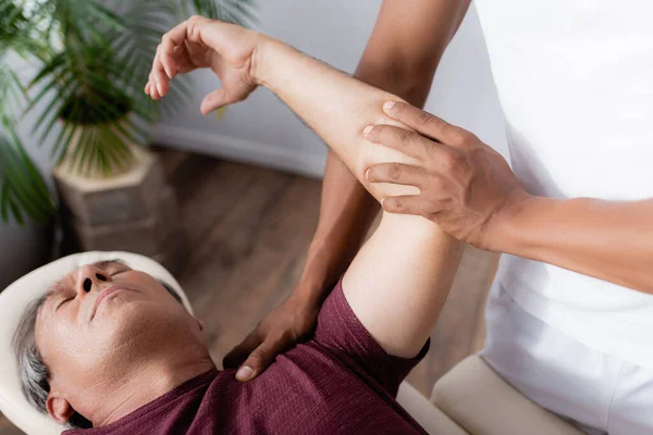 Quiropráctico afroamericano corregir brazo de hombre en mesa de masaje - foto de stock