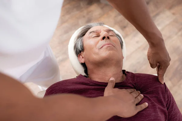 Vue grand angle de masseur afro-américain massant homme d'âge moyen sur table de massage — Photo de stock